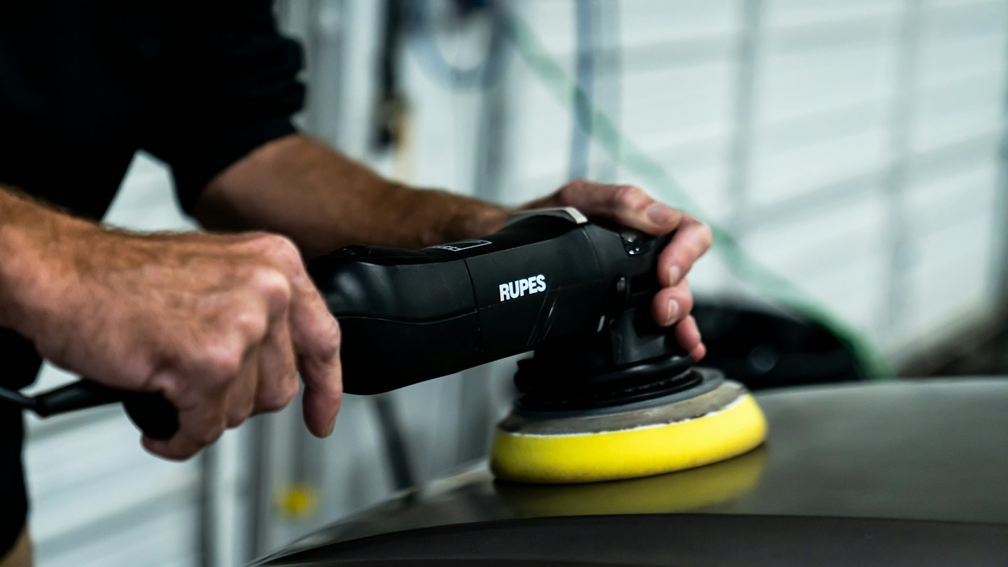 Hands use an orbital polisher on a car hood.