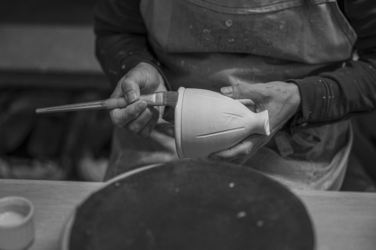 Potter painting glaze onto a ceramic vase in a workshop.