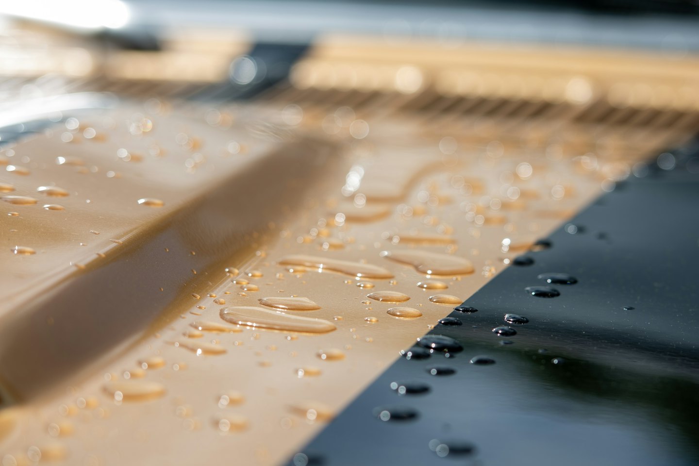 Clear water droplets bead on a shiny golden car hood.
